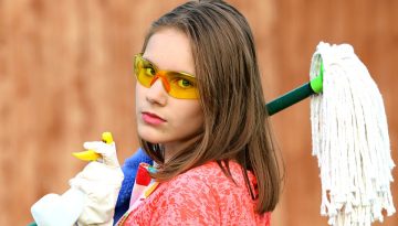 Girl with glasses holding a mop and spray bottle for house cleaning